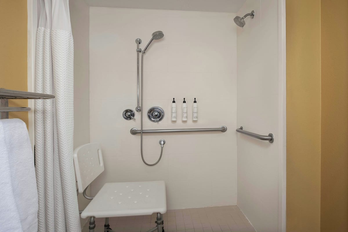 A shower area with a grab bar, a white chair, and a shelf with toiletries.
