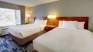 A hotel room with two beds, a wooden headboard, bedside lamps, and a large window with curtains.