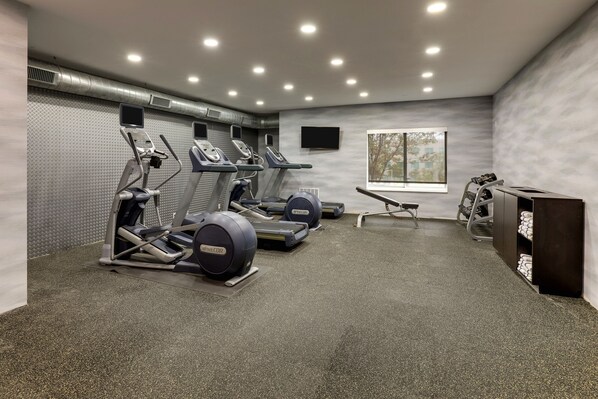 Un gimnasio con cintas de correr, elípticas y una máquina de remo.