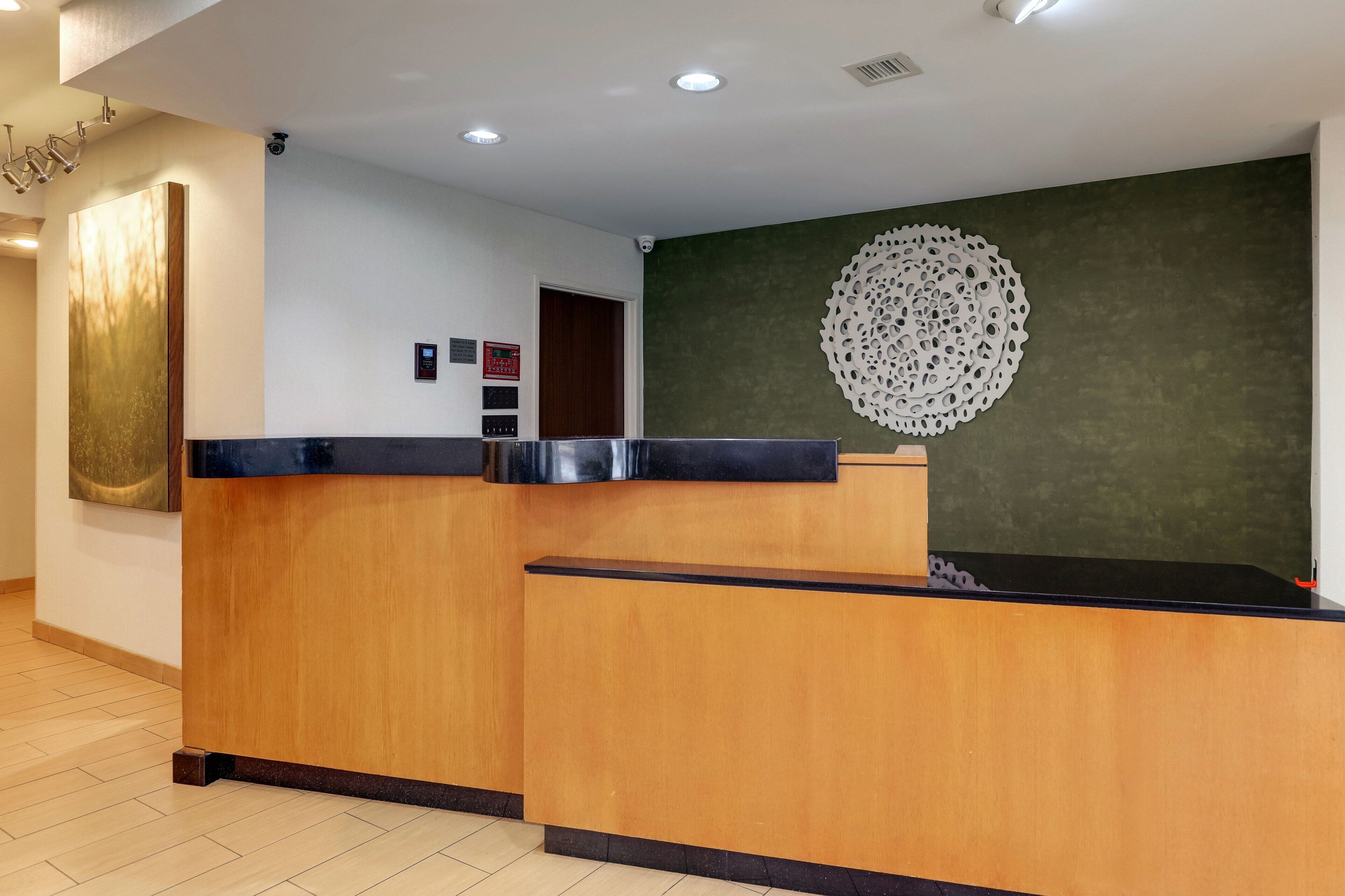 A reception desk with a wooden finish and a black top, a large abstract painting on the left, and a decorative wall piece on the right.