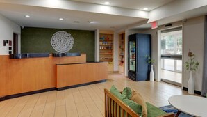 A reception area with a wooden reception desk, a green wall with a decorative pattern, a refrigerator, and a seating area with a table and chairs.