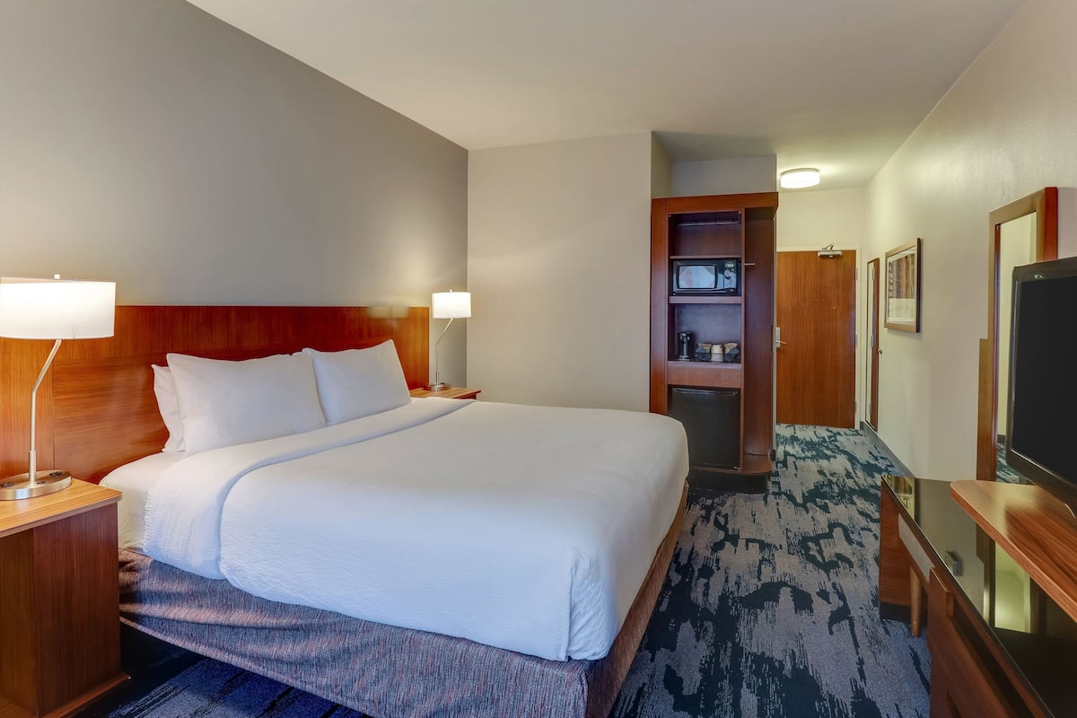 Ein Hotelzimmer mit einem großen Bett, einem Holzkopfbrett, zwei Nachttischlampen, einem Fernseher und einer kleinen Küchenzeile.