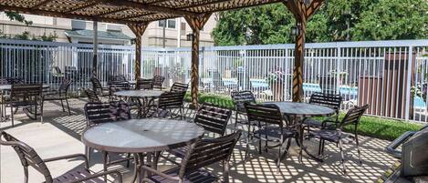 An outdoor patio area with round tables and chairs, a pergola structure, and a pool in the background.