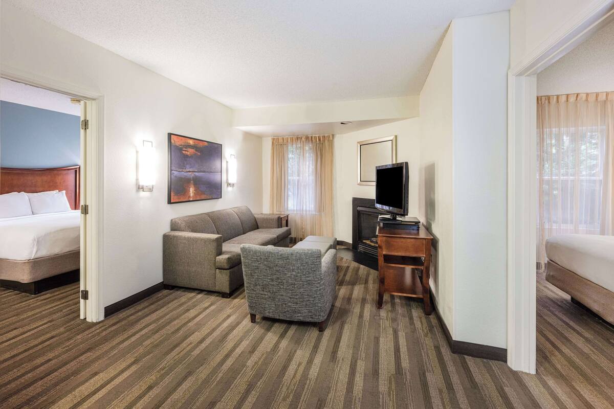 A hotel room with a bed, a sofa, a chair, a TV, and a fireplace.