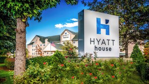 Letrero de Hyatt House con una H grande, rodeado de exuberante follaje y un edificio al fondo.
