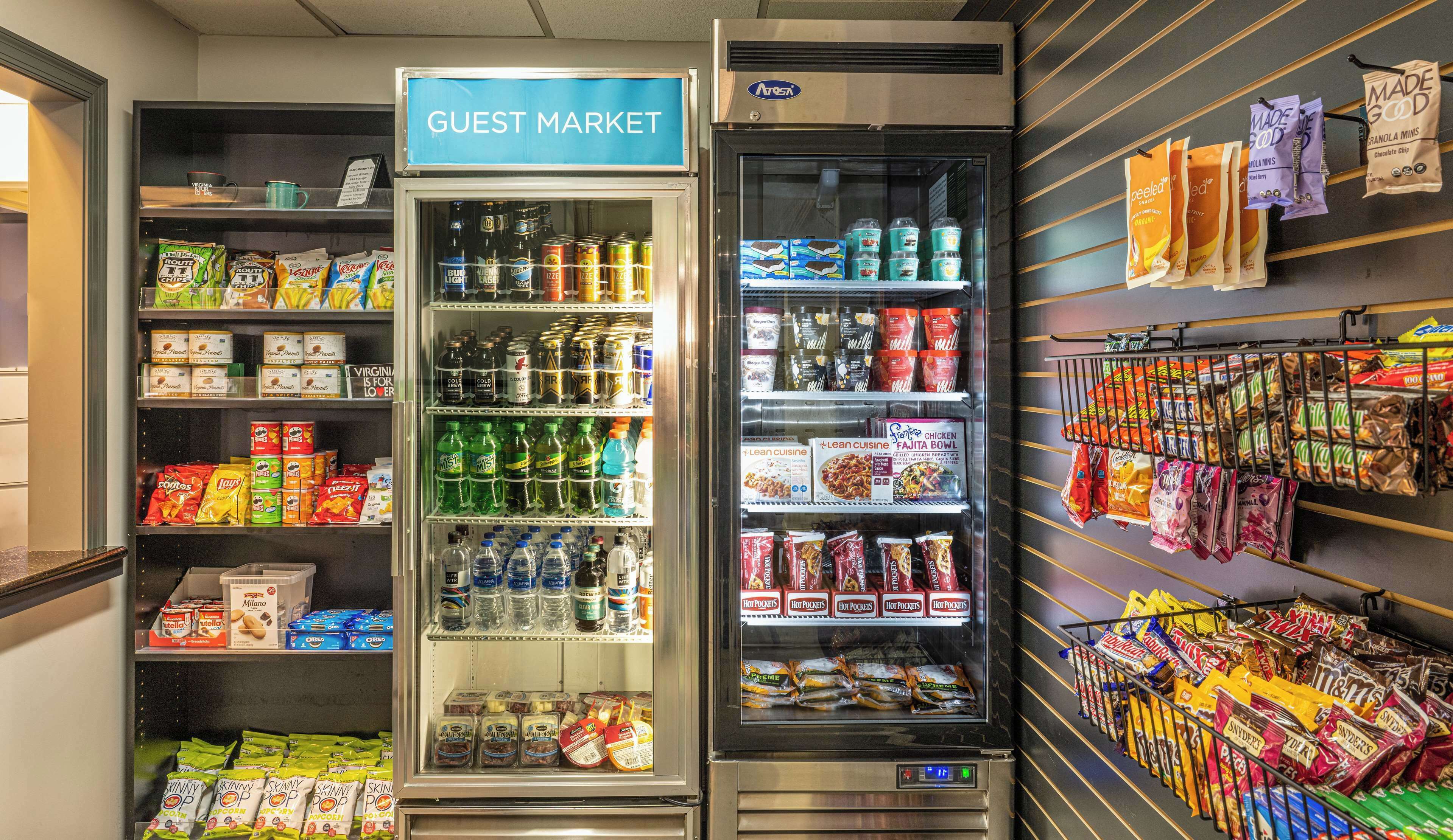 Un mercado para huéspedes con secciones refrigeradas y estantes llenos de bocadillos, bebidas y productos envasados.