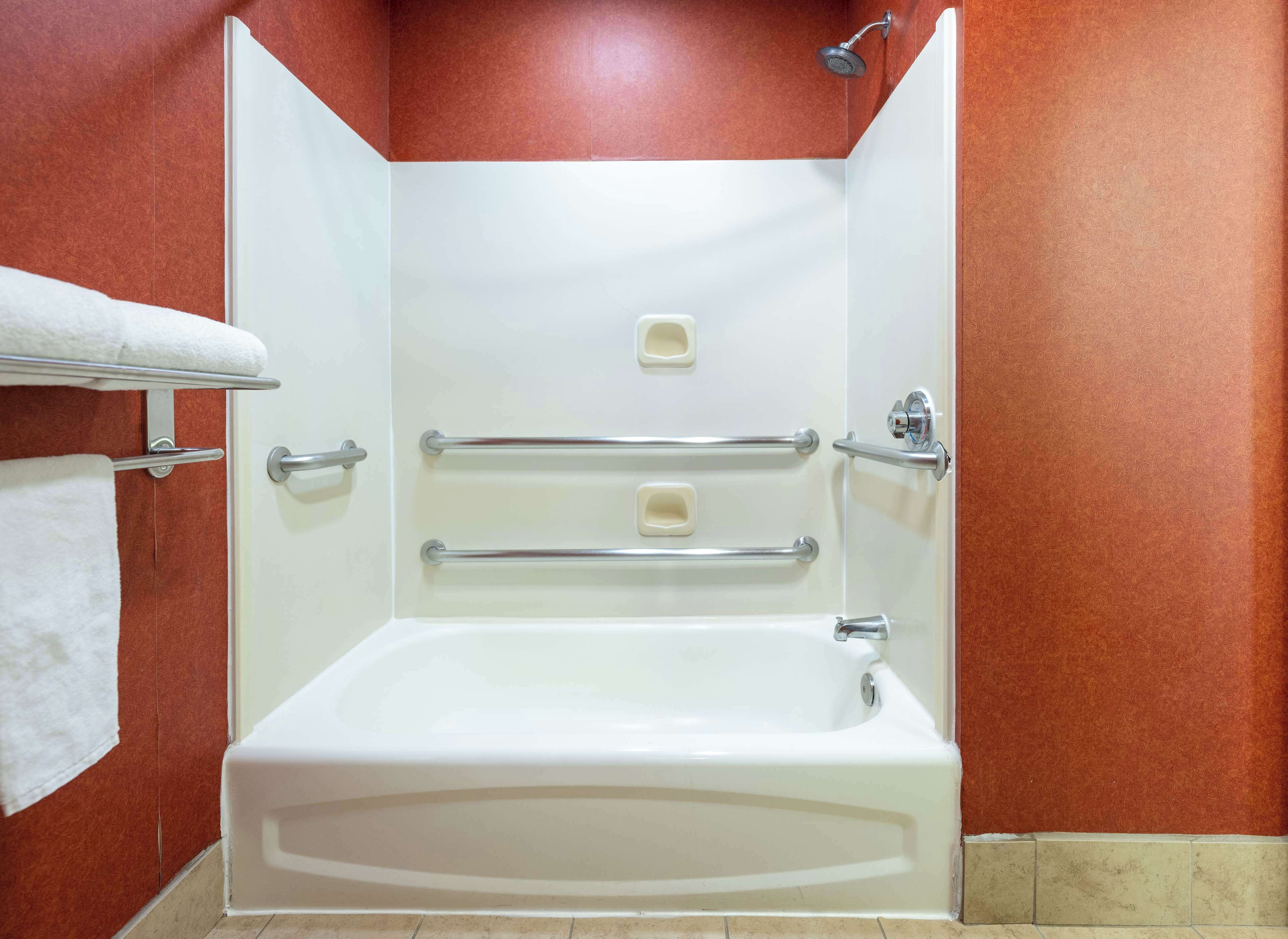 Una bañera blanca con dos barras de apoyo y un cabezal de ducha, frente a una pared roja.