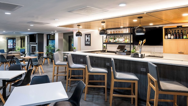 Zona de bar moderna con mostrador, taburetes y una variedad de botellas.