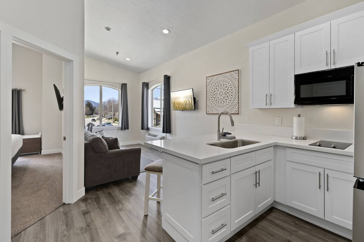 A modern kitchen with white cabinetry, a black microwave, and a large window.