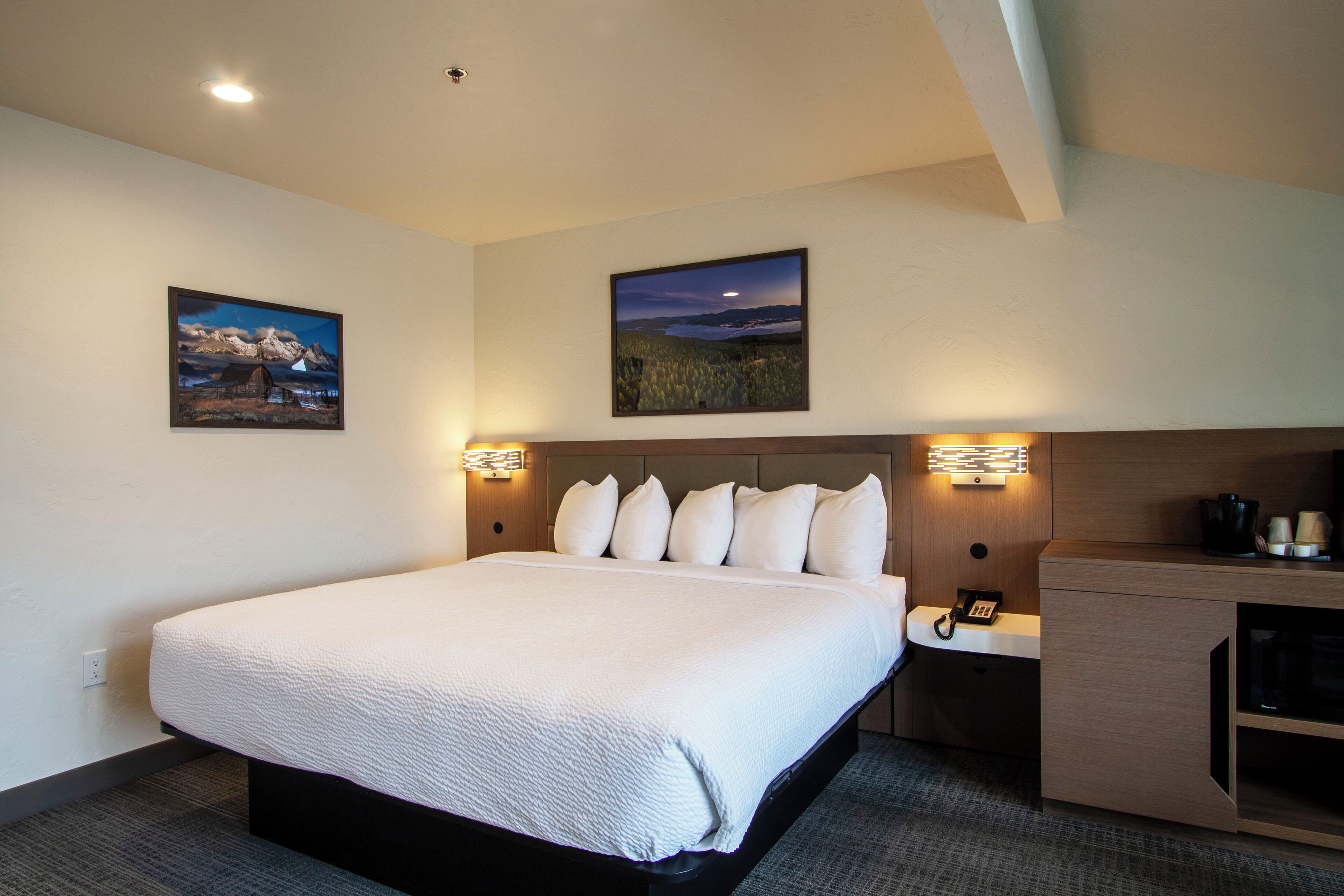 A hotel room with a large bed, two wall-mounted lamps, a nightstand with a phone, and two framed pictures on the wall.