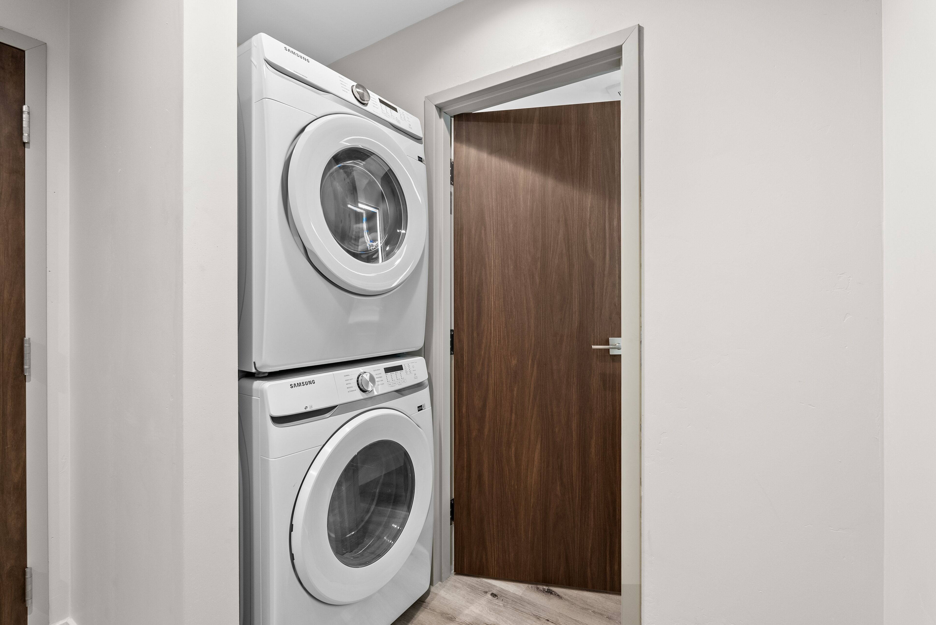 A laundry room with two stacked washing machines and a wooden door.