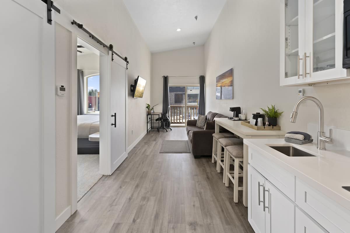 A modern kitchen with a dining area, a sliding door leading to a balcony, and a view of the outdoors.