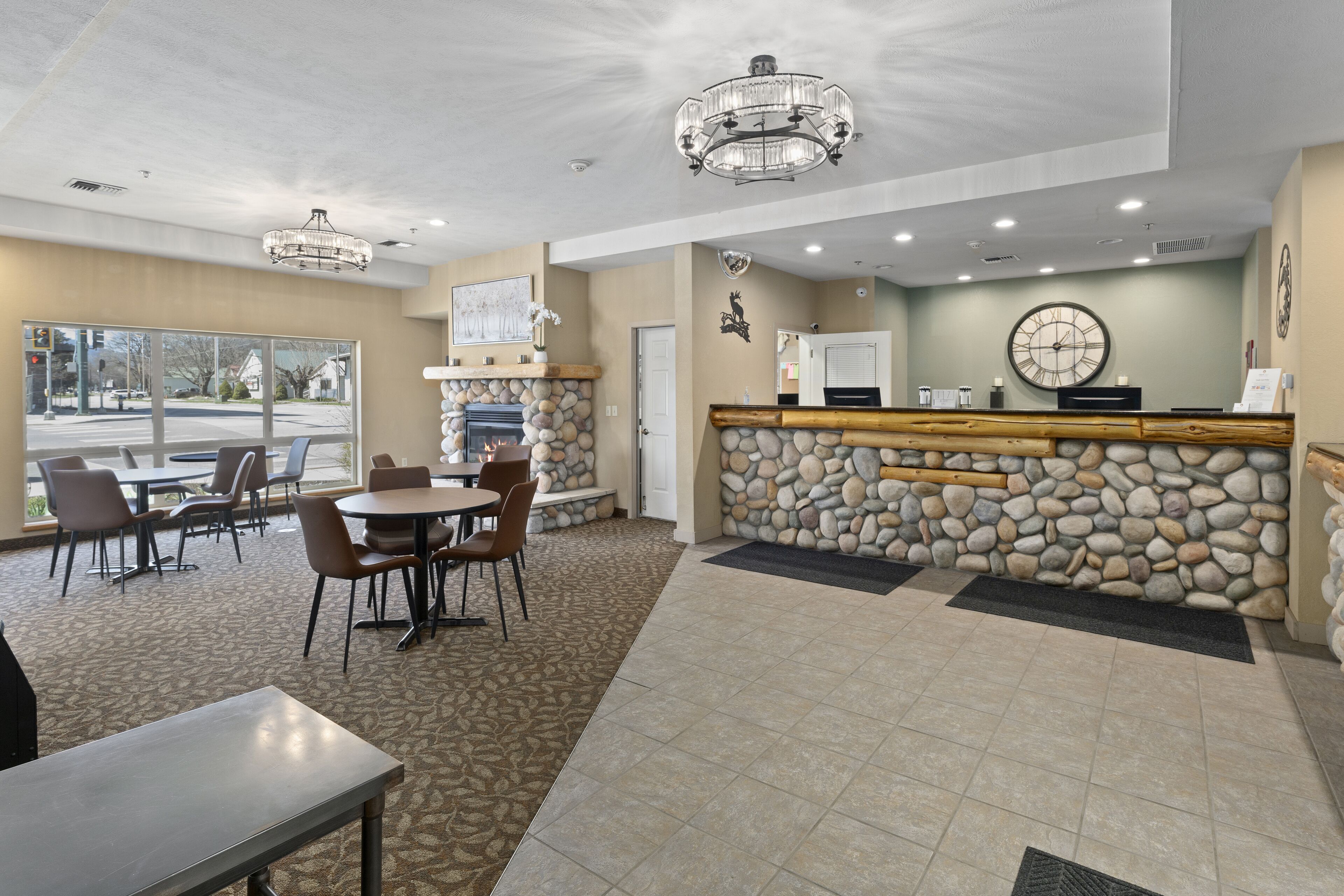 A lobby with a stone wall, a reception desk, and a fireplace. There are chairs and tables arranged for guests.