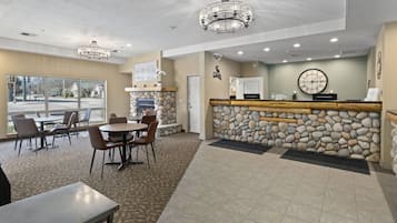 A lobby with a stone wall, a reception desk, and a fireplace. There are chairs and tables arranged for guests.