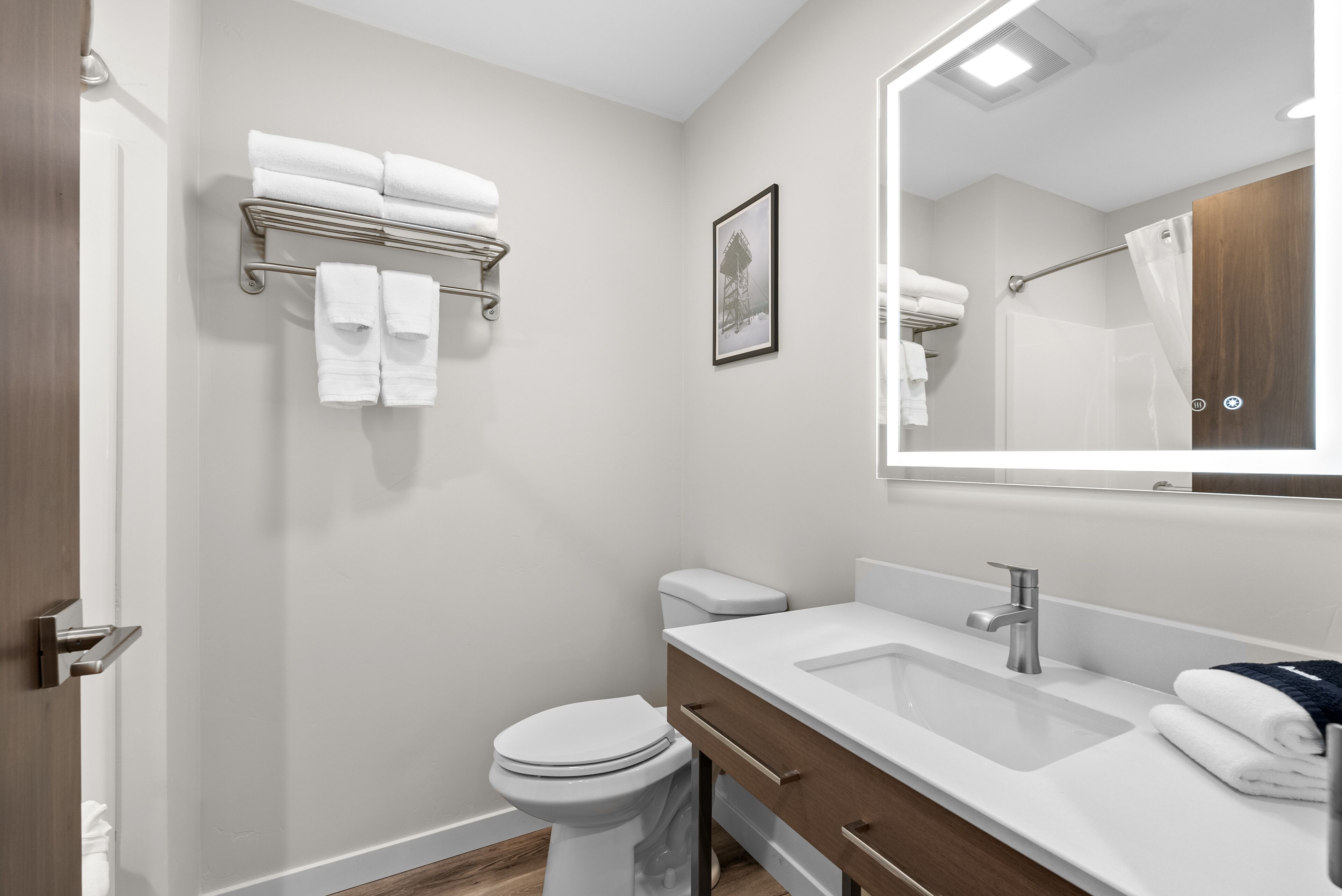 A modern bathroom with a white toilet, a sink with a mirror, and a towel rack with folded towels.