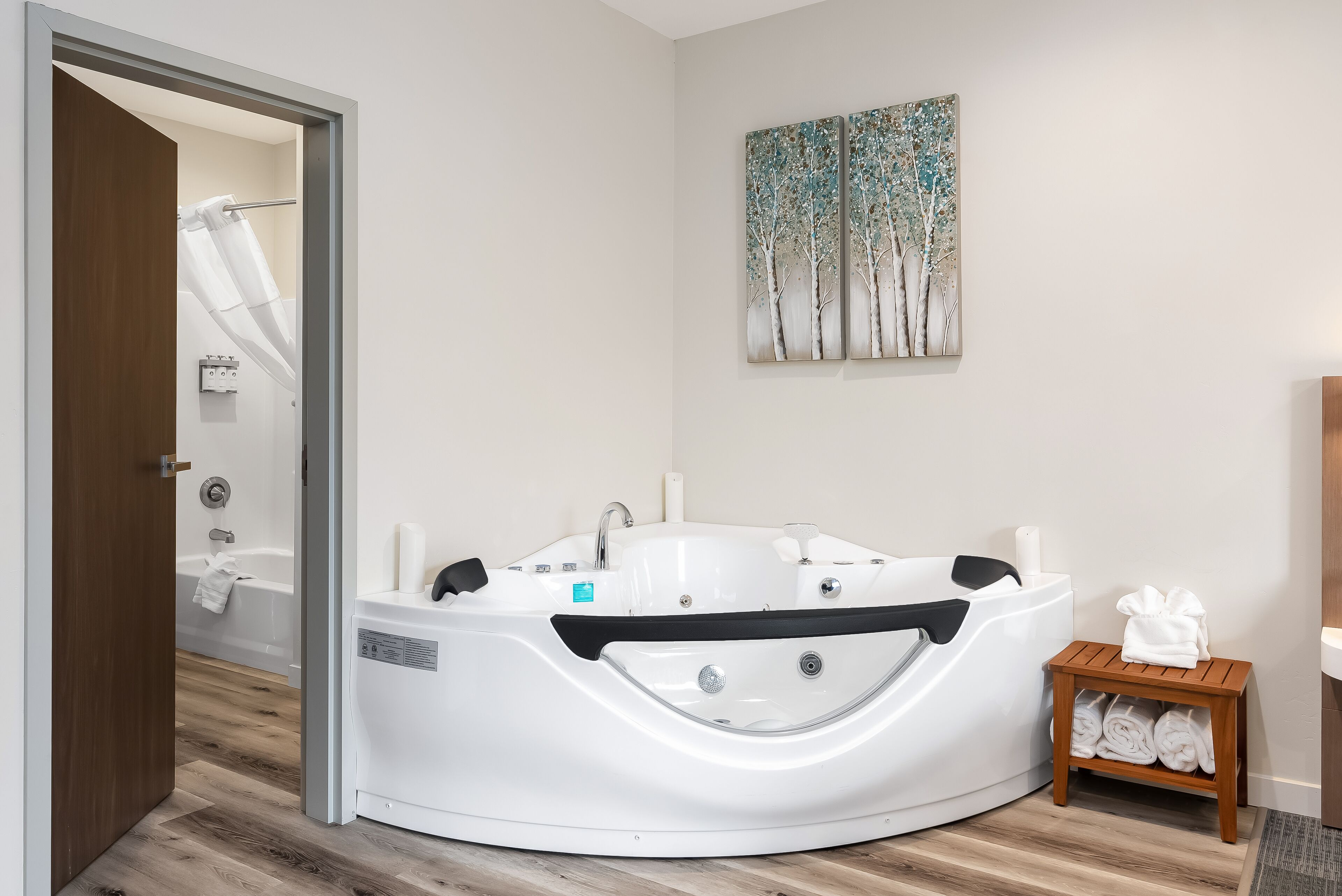 A modern bathroom with a freestanding bathtub, a wooden bench with towels, and a wall-mounted painting.