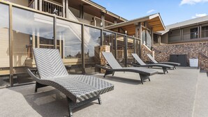 A building with a covered outdoor seating area featuring lounge chairs and a stone wall. - Sandpoint Hotel & Suites Downtown (Sandpoint)