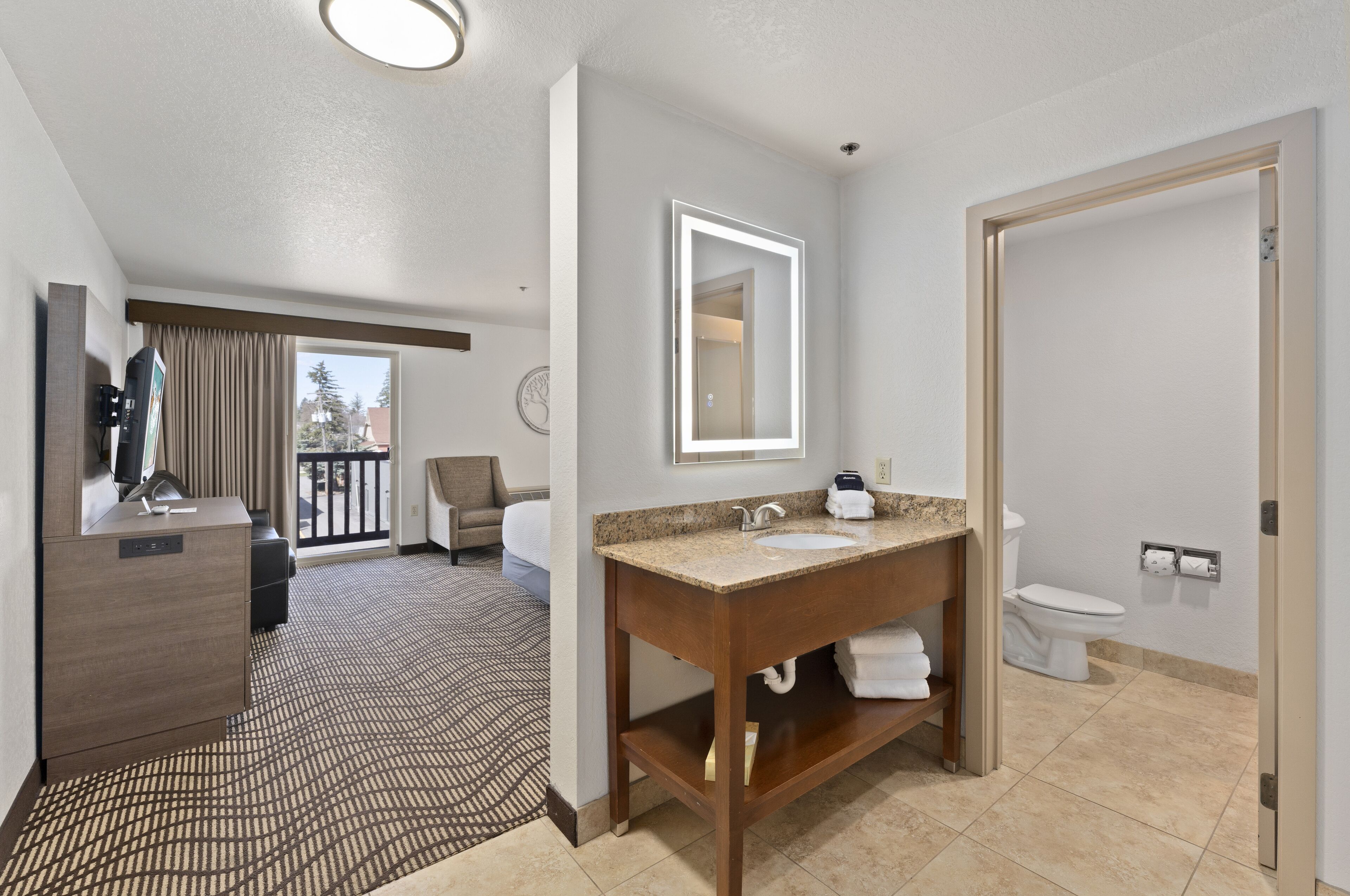 A hotel bathroom with a wooden vanity, a large mirror, a sink, and a toilet.