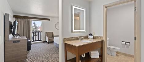 A hotel bathroom with a wooden vanity, a large mirror, a sink, and a toilet.