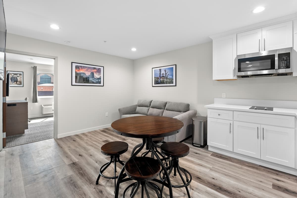 A modern kitchen with white cabinets, a built-in microwave, and a round wooden dining table with four stools.