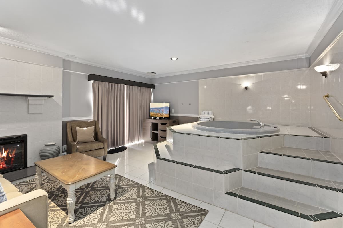A modern hotel room with a fireplace, a seating area, a large bathtub, and a staircase leading to a private balcony.