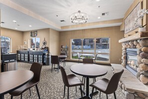 A restaurant with round tables and chairs, a bar area, and a stone fireplace. - Sandpoint Hotel & Suites Downtown (Sandpoint)
