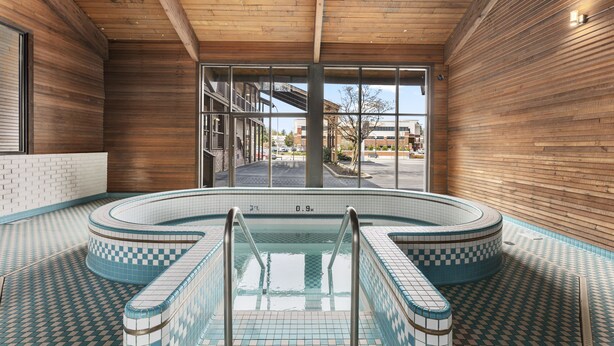 An indoor swimming pool with checkered blue and white tiles, metal handrails, and a view of the outside through large windows. - Sandpoint Hotel & Suites Downtown (Sandpoint)