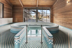 Une piscine intérieure aux carreaux bleus et blancs, dotée de rampes métalliques et offrant une vue sur l’extérieur grâce à de grandes fenêtres.