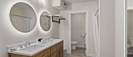 Une salle de bain moderne avec un meuble-lavabo à deux vasques, un grand miroir et des toilettes visibles au fond.