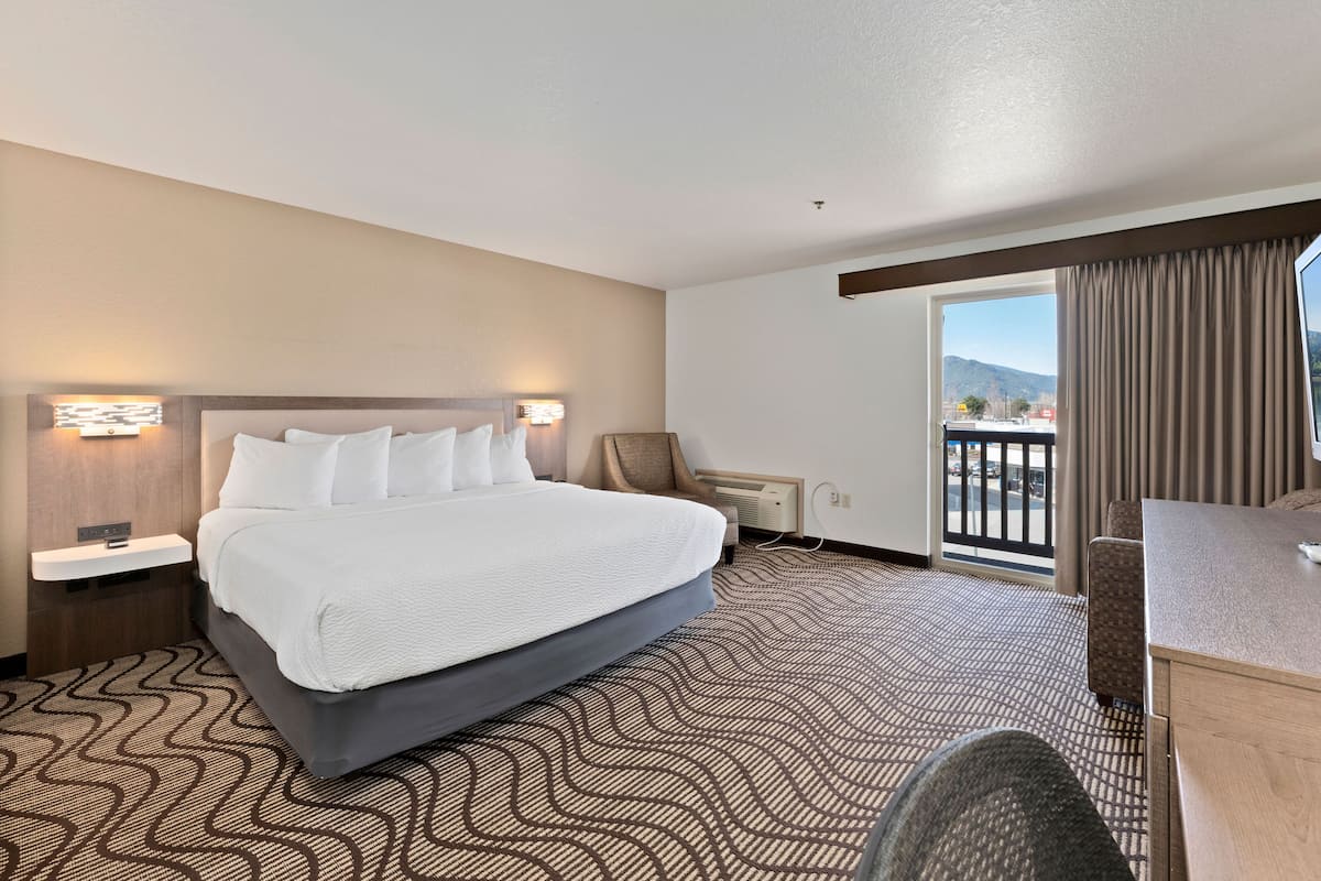 A hotel room with a large bed, a desk, a chair, and a view of the mountains through the window.