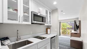 A modern kitchen with white cabinetry, a stainless steel sink, a built-in microwave, and a compact refrigerator. - Sandpoint Hotel & Suites Downtown (Sandpoint)