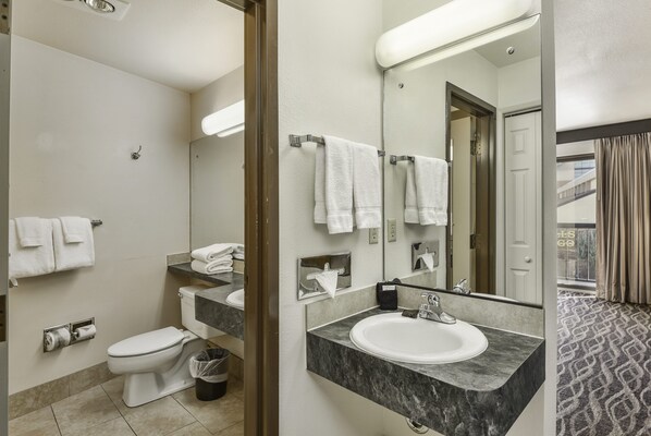 Une salle de bain moderne avec des toilettes, un lavabo et un grand miroir. Plusieurs serviettes sont suspendues sur un porte-serviettes, et il y a une poubelle.