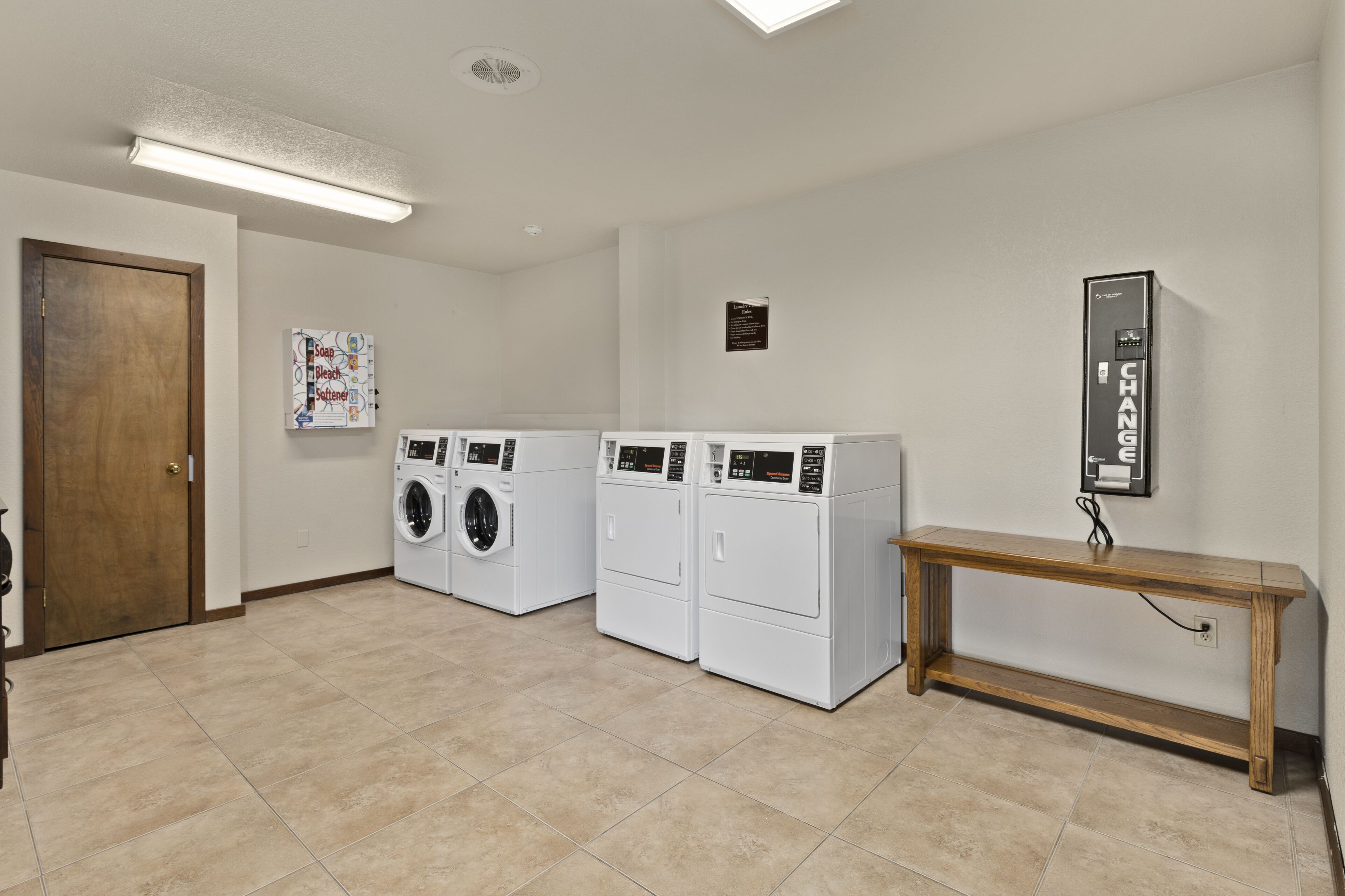 A laundry room with three stacked washers and dryers, a wooden bench, and a wall-mounted control panel.