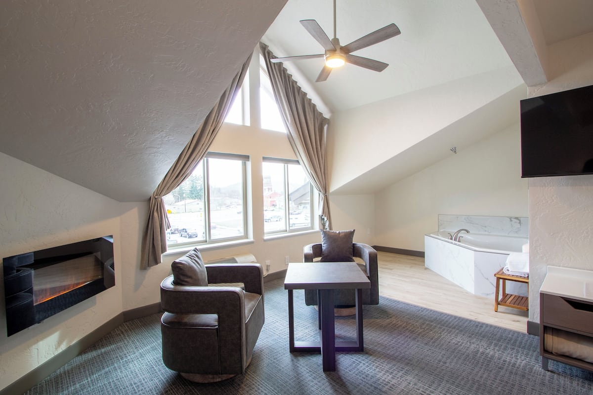 A modern living room with a fireplace, a ceiling fan, and a large window with curtains.
