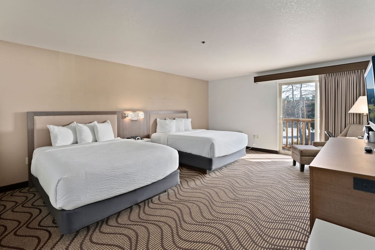 A hotel room with two beds, a desk, and a view of the outdoors.