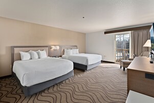 A hotel room with two beds, a desk, and a view of the outdoors.