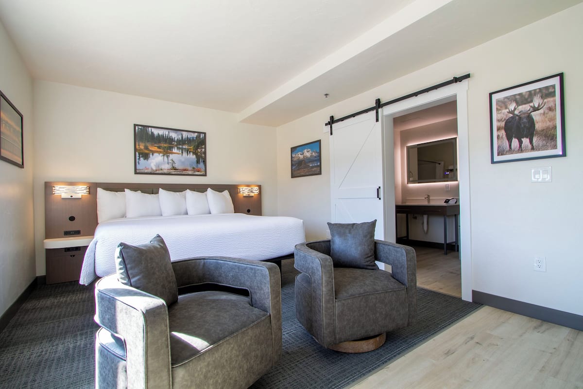 A hotel room with a large bed, two armchairs, a desk, and a bathroom visible through an open door.