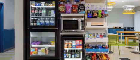Zona de venta con diversas opciones de aperitivos, un microondas y un refrigerador lleno de bebidas.