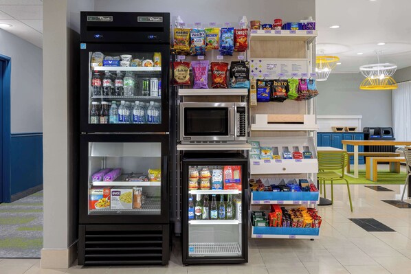 Zona de venta con diversas opciones de aperitivos, un microondas y un refrigerador lleno de bebidas.