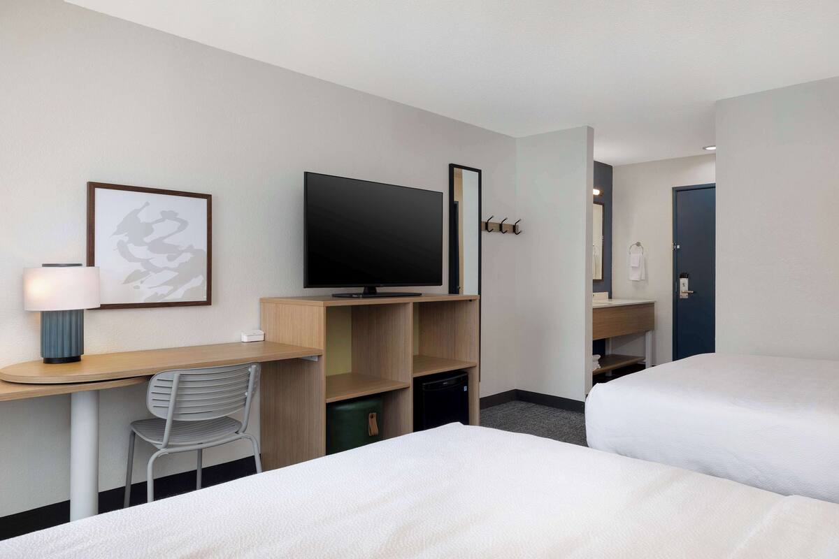 A hotel room with a bed, a desk with a television, a chair, and a small cabinet.