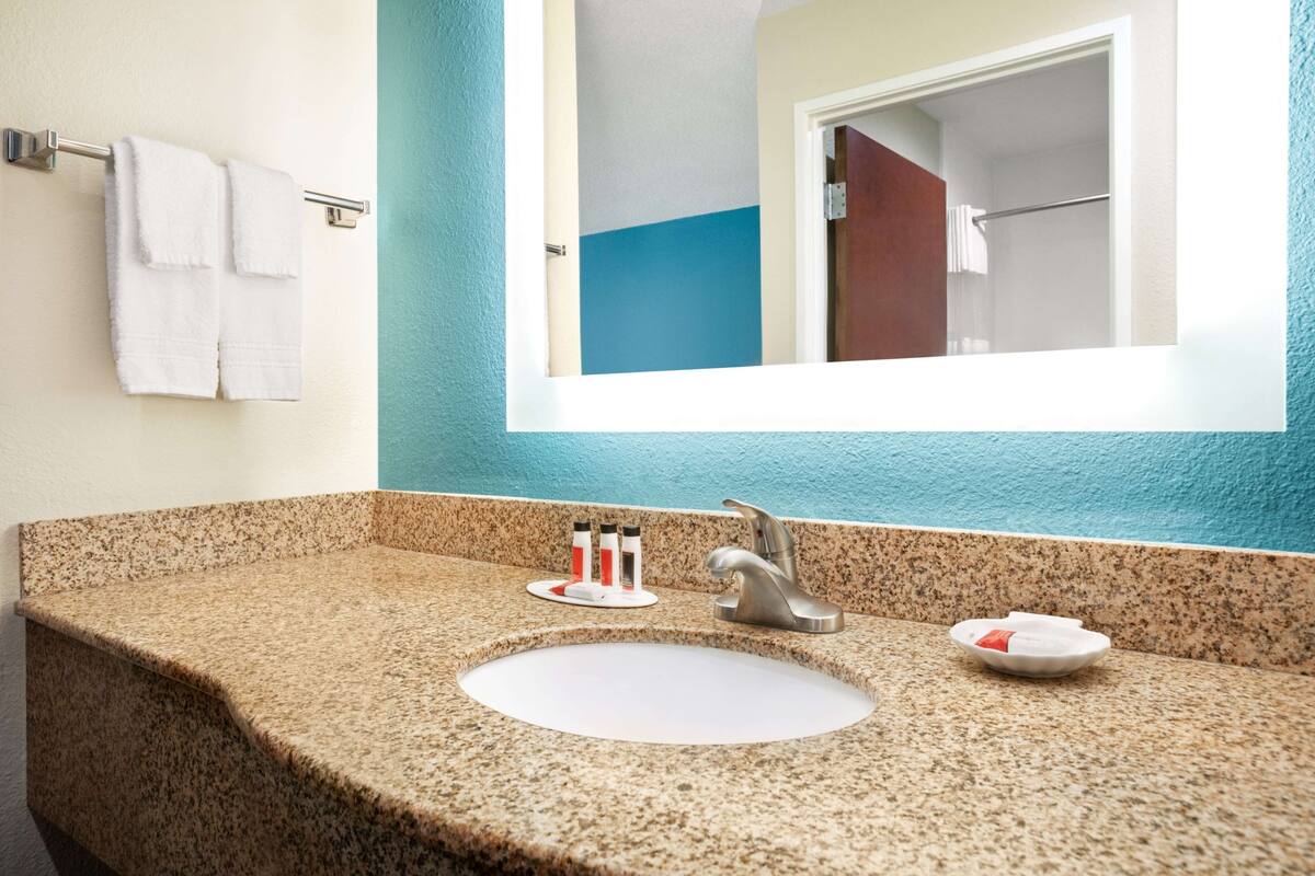 A bathroom with a granite countertop, a white sink, a mirror, and a towel rack.
