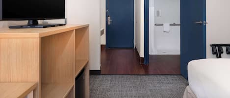 Quarto de hotel com cama, escrivaninha com televisão, banheiro com banheira e porta que dá para outro quarto.