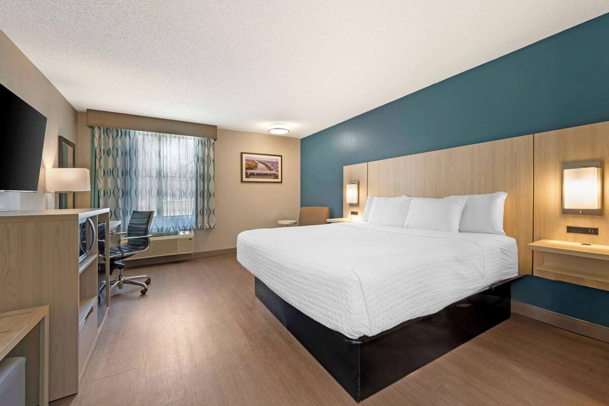 A hotel room with a large bed, a desk with a chair, a television, and a window with curtains.