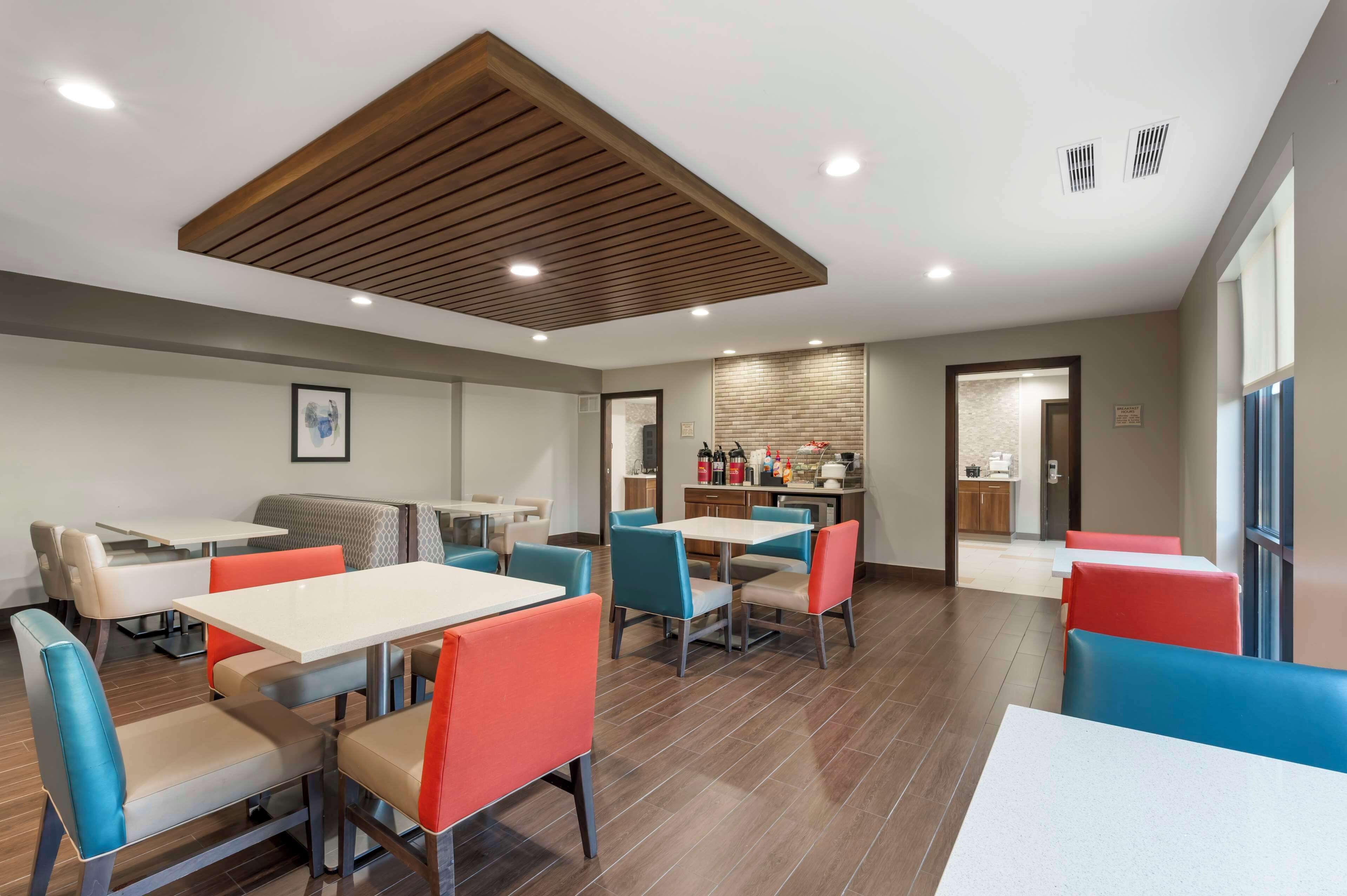 A modern dining area with multiple tables and chairs, a kitchen in the background, and a wooden ceiling design.
