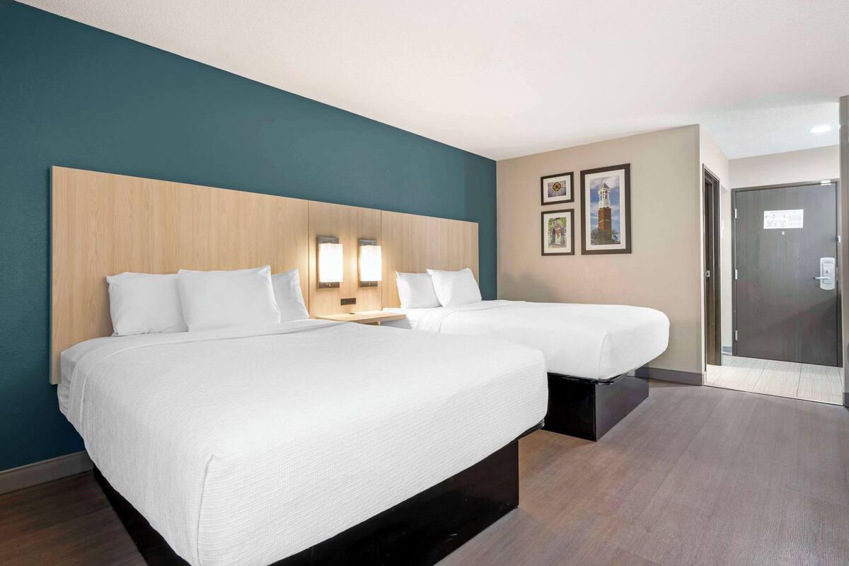 A hotel room with two beds, a wooden headboard, white bedding, and a teal accent wall.