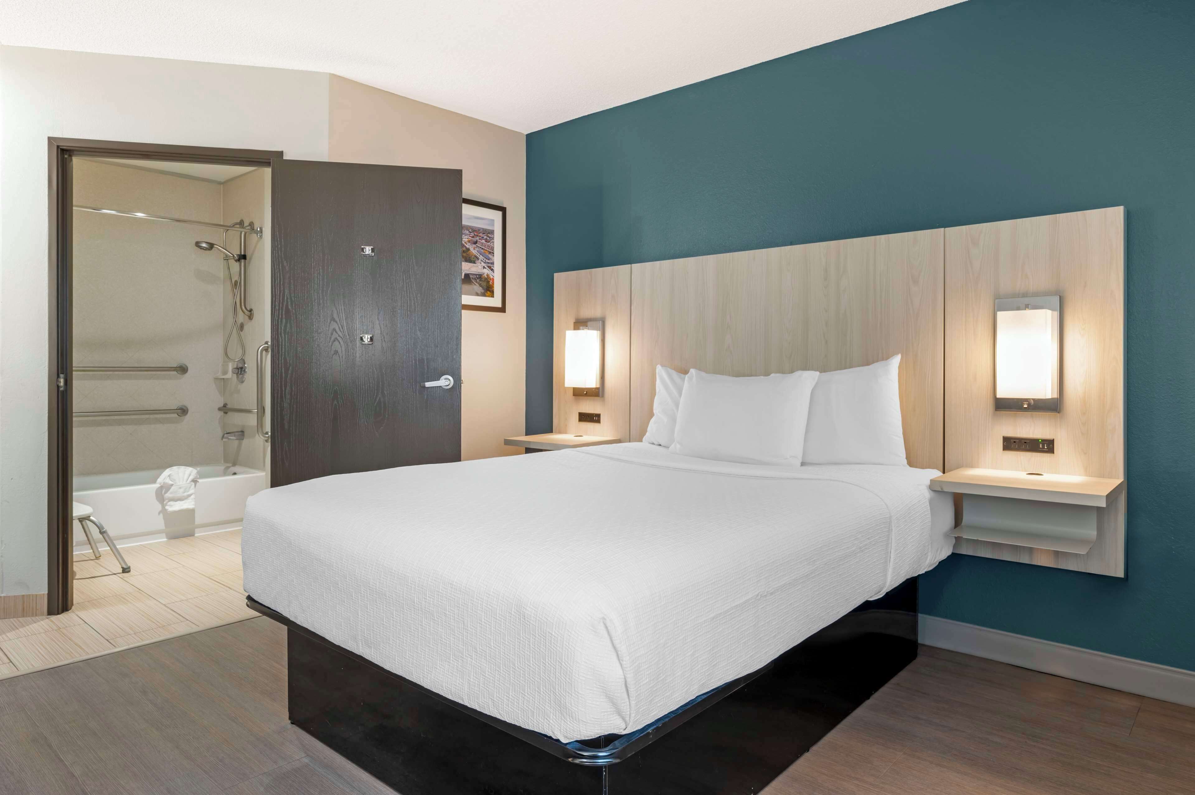 A hotel room with a large bed, two bedside tables with lamps, a shower area, and a door to the bathroom.