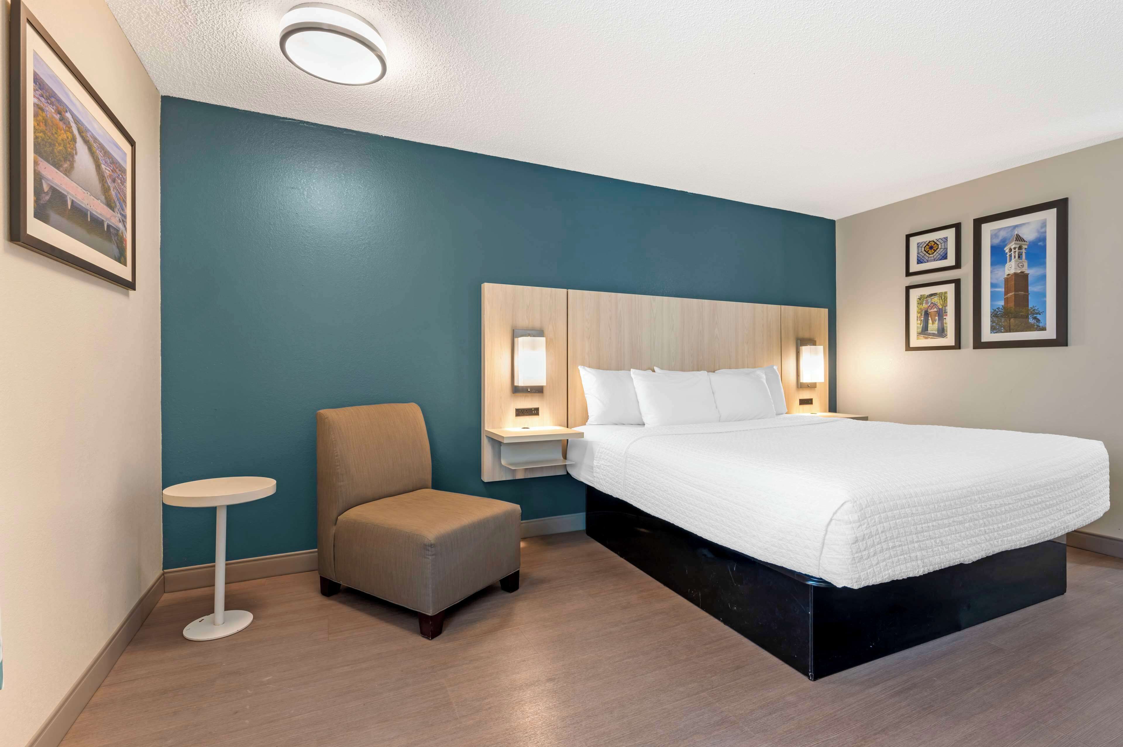 Une chambre d’hôtel avec un grand lit, une petite table ronde, une chaise et une table de chevet avec une lampe.
