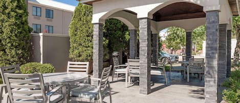 Un patio exterior con zona de estar cubierta, pilares de piedra y una mesa con sillas.