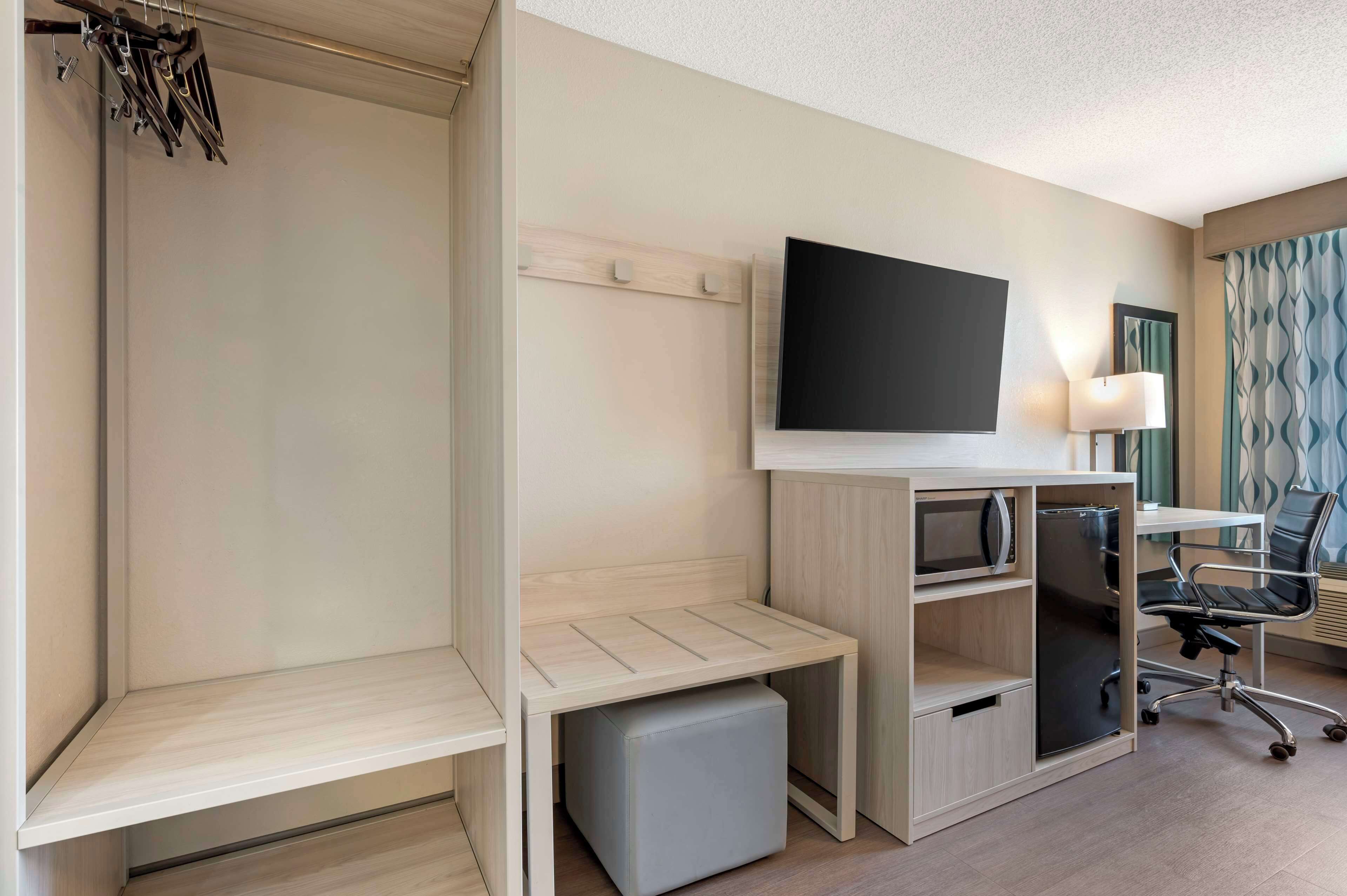 A hotel room with a bed, a TV, a desk with a chair, a lamp, and a wardrobe.