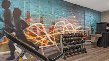 Une salle de sport équipée de matériel d’exercice, un mur orné d’œuvres d’art abstrait et un porte-haltères.